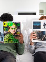 Two people sitting on a bed reading magazines