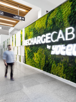 A man walks by a green wall within an airport with large block writing, Recharge Cabins by YOTEL