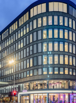 High-rise hotel facade at night with bright lights on in every room, including a dazzling purple lobby glowing upon the traffic outside