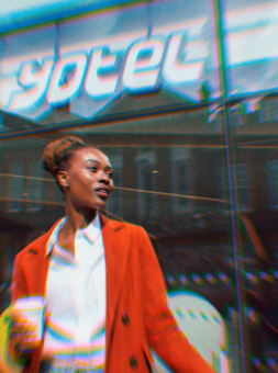 Glamorous woman in a red coat stands outside the glass facade of YOTEL hotel lobby