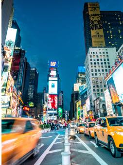 A buzzing view of times square, surrounded by speeding yellow taxis at night