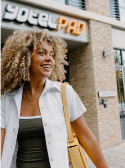 A curly haired woman smiles outside YOTELPAD London Stratford's exterior
