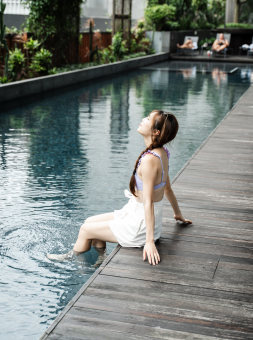 A woman dips her feet into an outdoor pool surrounded by plants