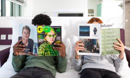 Two people sitting on a bed reading magazines