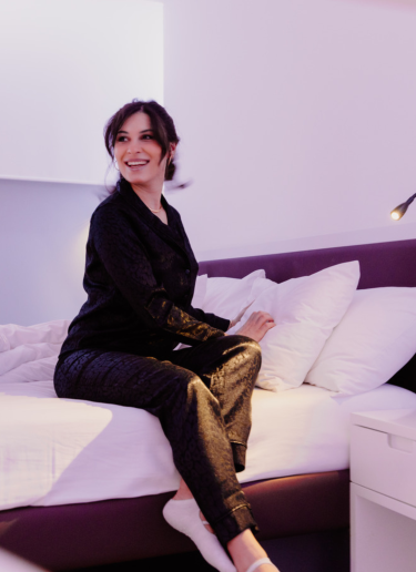 Woman dressed in smart attire sits on her hotel room bed, crossing her legs