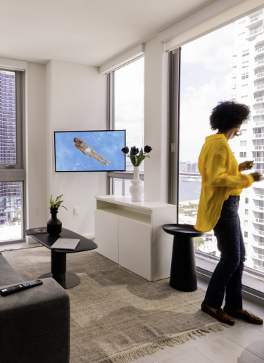 A woman in a yellow top looks out the window from her studio pad lounge area