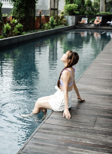 A woman dips her feet into an outdoor pool surrounded by plants
