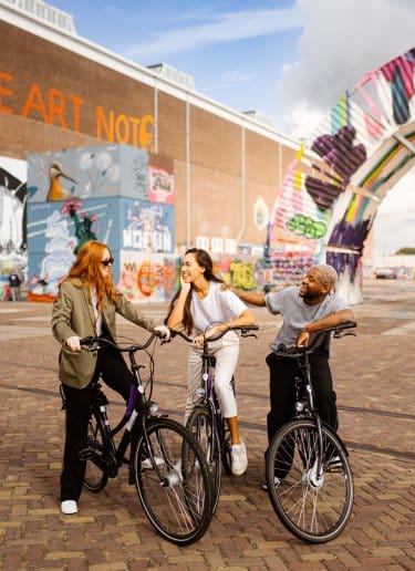 Three people cycling through an eclectic street in Amsterdam