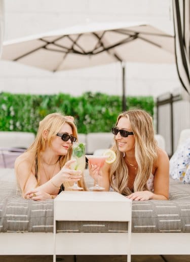 Two girls relax on a sun lounger and chat over cocktails