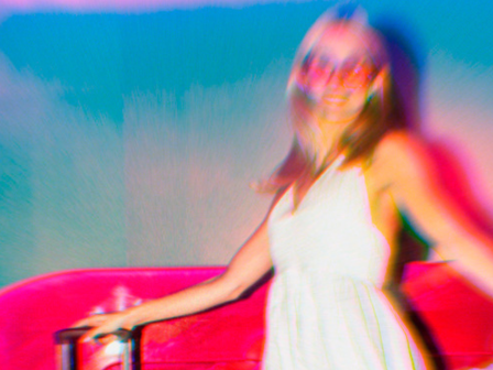 Woman in a white summer dress and sunglasses confidently strolls by holding her luggage