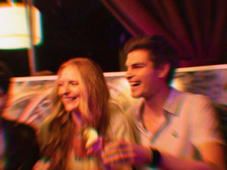 A couple relax on a double seater in a restaurant and laugh at a performance out of shot