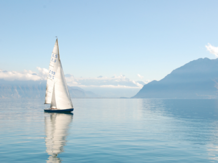 A yacht sails across a still lake with Alpine mountains in the background