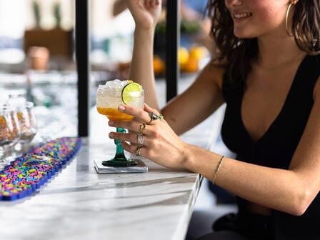 A woman in a black dress holding an orange cocktail at a bar