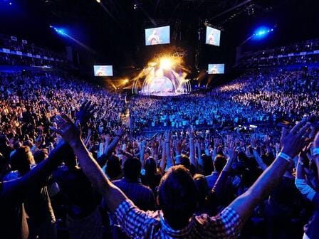 A huge crowd gather for a dynamic concert with bright lights and an energetic atmosphere