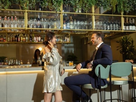 A man and a woman chat at a well-stocked trendy bar