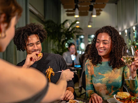 Three adults laughing over a meal in a dimly lit restaurant 