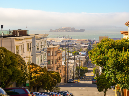 A bright street-view scene of suburban San Francisco with Alcatraz seen in the distance