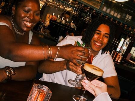 A group of friends clinking glasses in a vibrant, dimly lit bar