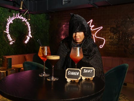 Woman in black cloak with drinks in front on a table