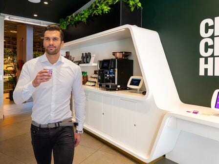 Man standing with coffee cup in front of food and drink display