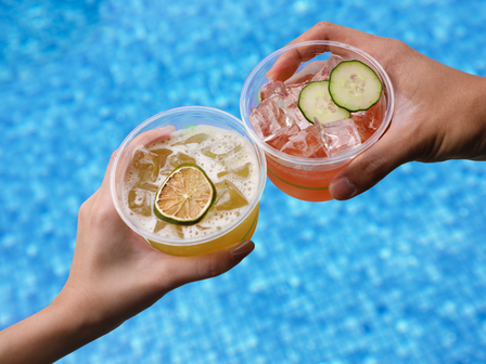Two hands with cocktails held over a swimming pool
