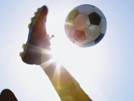 A man kicking a football into the sun