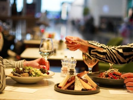 Two people in shirts enjoy a glass of wine and a meal at a fancy restaurant