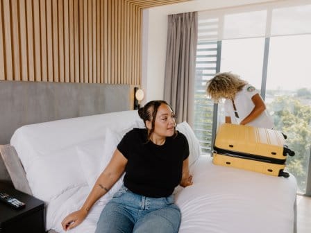 Two women unpacking their suitcase in a bright hotel room bed
