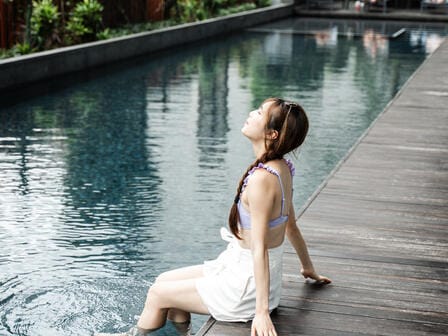 A woman dips her feet in an ourdoor hotel pool, surrounded by greenery