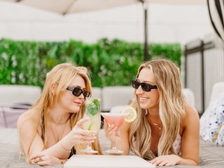 Two girls relax on a sun lounger and chat over cocktails