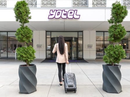 A smartly dressed woman approaches a hotel lobby with her suitcase