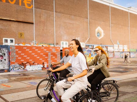 Three people cycling through an eclectic street in Amsterdam
