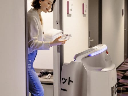A woman greets a robot at her hotel room door