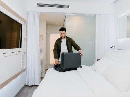 A man unpacks his suitcase in a clean hotel room
