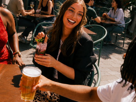Woman smiling and holding a cocktail outside with man in the foreground