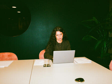 A woman sits alone in a room with a laptop