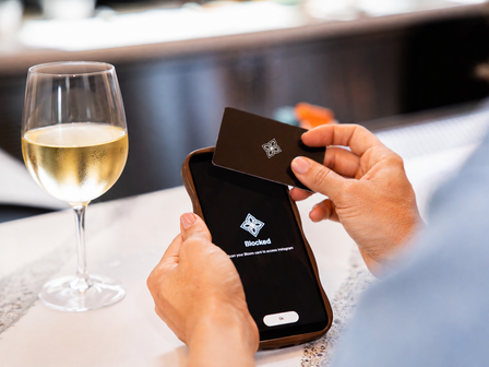 A man taps a card to his mobile photo with a glass of white wine