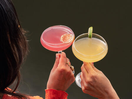 Two women holding colourful cocktails with canal in the background