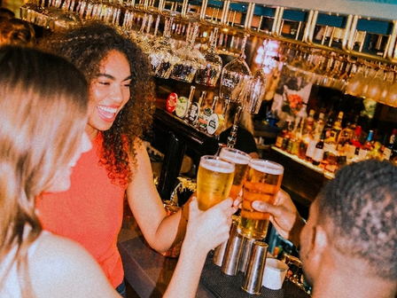 Group of two women and a man cheersing with pints of lager