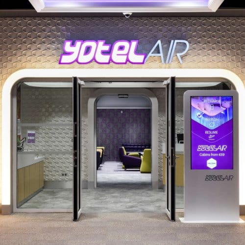 Entrance lobby to an airport hotel with digital display screen, a check-in desk and glowing YOTELAIR lettering 