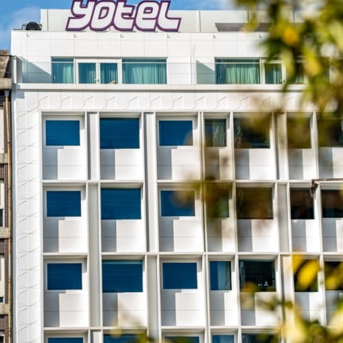 Blue sky and green trees overlooking the white facade of YOTEL Porto
