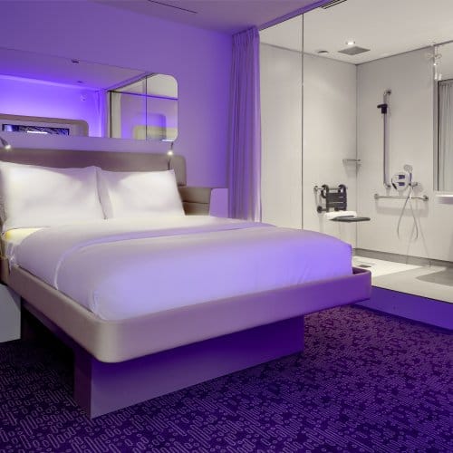 A large purple hotel room with mood lighting, a bright ensuite bathroom and mirror