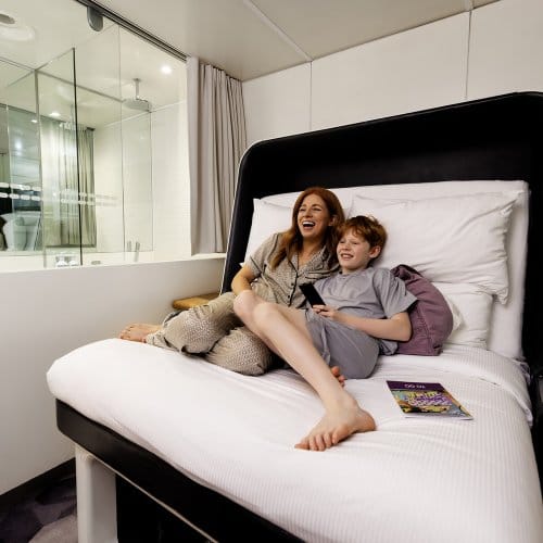 A mother and her son lie back in bed laughing, watching a show on TV