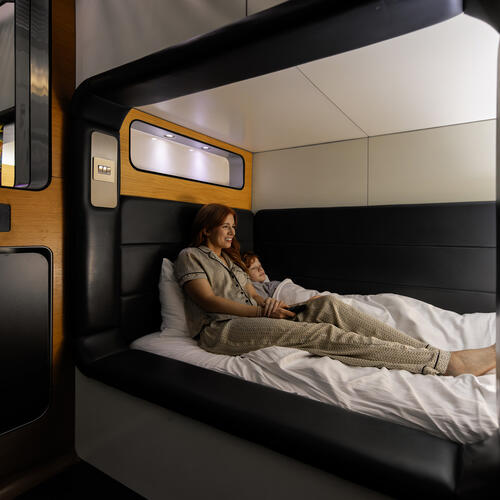 A woman and her child fall asleep in a single-bed while the TV plays