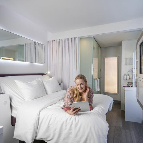 Woman lying on bed in a smart, clean hotel room and reading a tablet