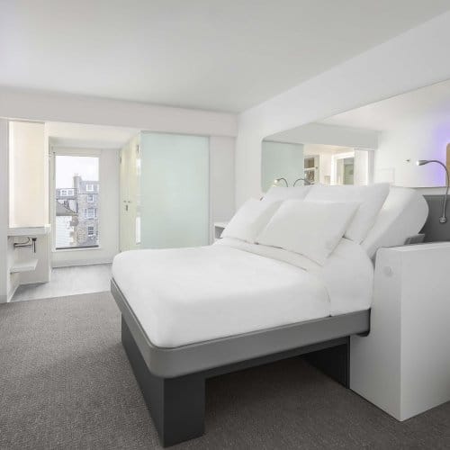A large well-lit hotel room with a big bed, TV screen, bathroom and floor-to-ceiling windows