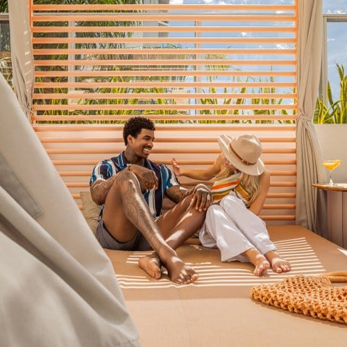 A man and a woman relax on a poolside cabana in the sun