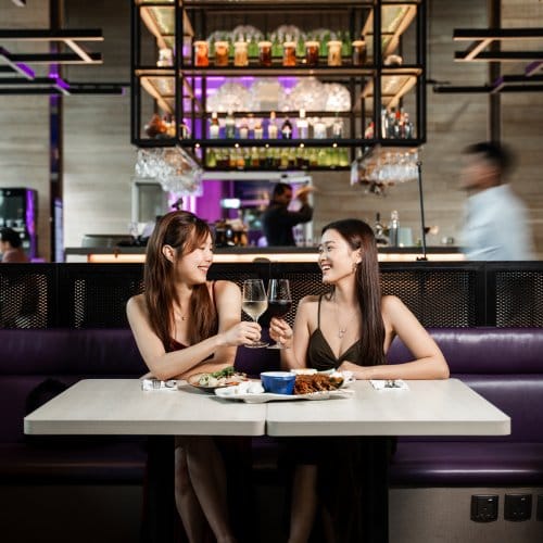 Two woman click their glasses over a meal in a trendy hotel restaurant and bar