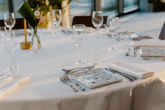A round table with white cloth, wine glasses and formal cutlery presentation