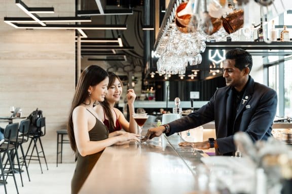 Two women ordering cocktails at a well-lit bar during the day